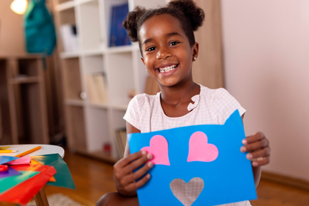 Beautiful little girl holding finished art project for school made of colorful papers